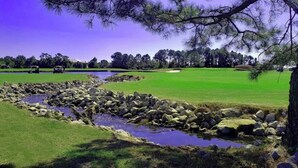Campo de golf con un estanque, árboles y cielo despejado.