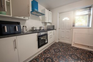 Una cocina con armarios blancos, una campana extractora azul, un microondas y baldosas de suelo con diseño.