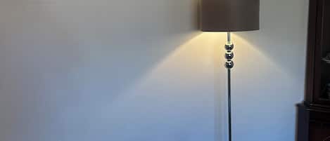 A floor lamp with a shade, a painting with abstract floral designs, and a dark-colored cabinet.