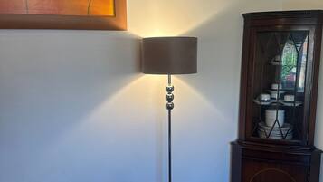A corner room with a standing floor lamp, a cabinet with glass doors, and a painting on the wall.