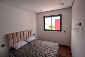 A bedroom with a bed, a window, and a wall-mounted light fixture. - Charming 2-Bedroom Apartment in the Heart of Martil, Morocco (Martil)
