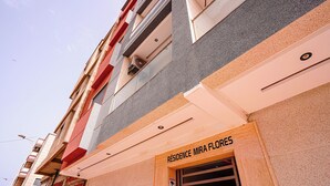 Rakennuksessa on kyltti, jossa lukee ”RESIDENCE MIRA FLORES”, ja lisäksi siinä on varoituskyltti, jossa kiinnitetään huomiota turvallisuuteen.
