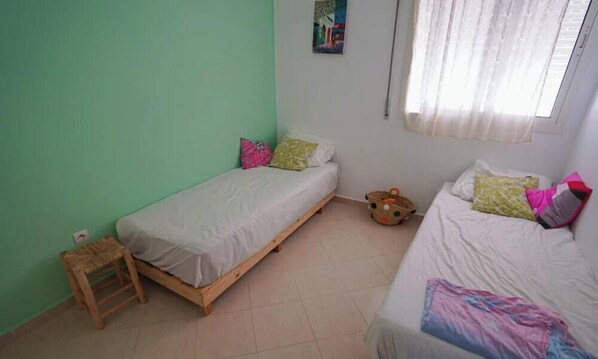 A room with two single beds, a small wooden stool, and a basket. - Charming 2-Bedroom Apartment in Martil, Morocco (Martil)