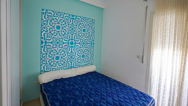 Ein Zimmer mit einem Bett, einer Wand mit Muster und einem Fenster mit Vorhängen.