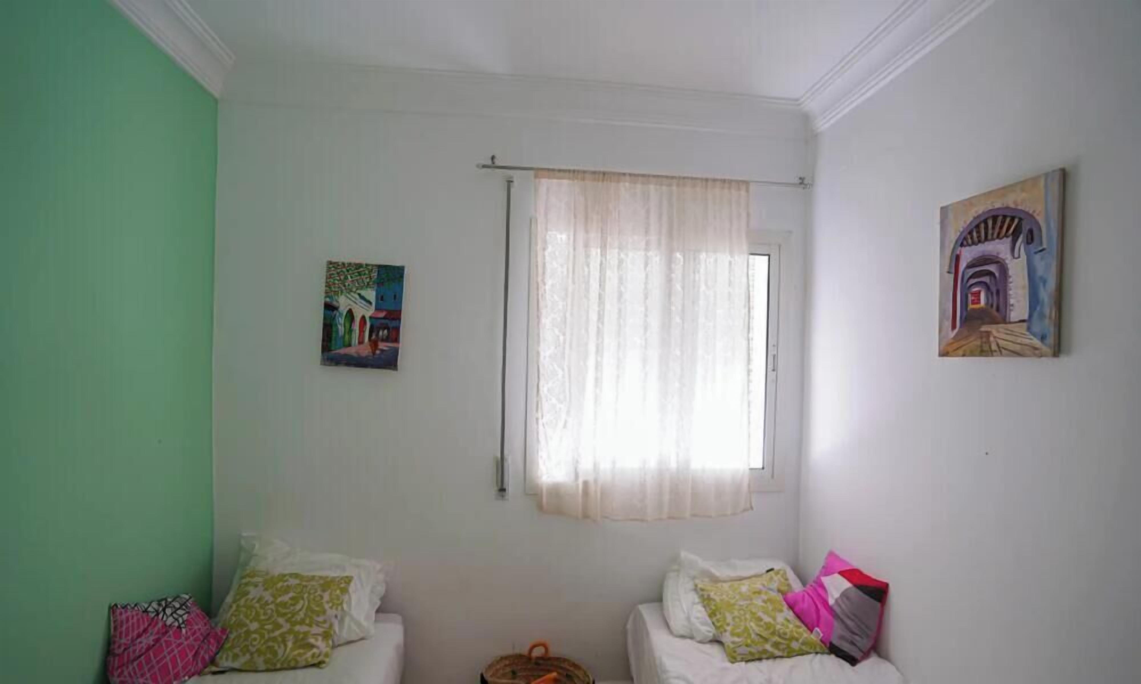 A room with two beds, a window with sheer curtains, and two paintings on the walls.