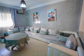 A living room with a sofa set, a dining table, and artwork on the walls. - Charming 2-Bedroom Apartment in Martil, Morocco (Martil)