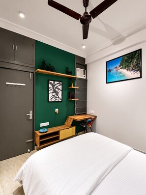 Quarto com cama, escrivaninha, ventoinha no teto, TV na parede e uma parede verde decorativa.