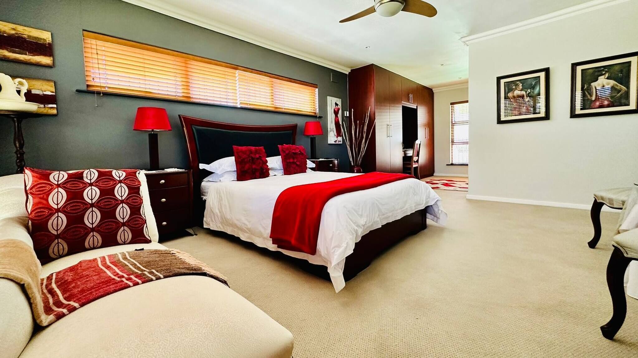 A bedroom with a large bed, a nightstand, a chair, a ceiling fan, and artwork on the walls.