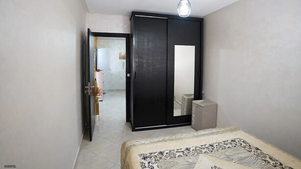 Quarto com cama, guarda-roupa, espelho e luminária pendente.