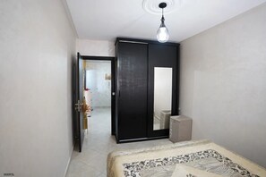 A bedroom with a bed, a wardrobe, a mirror, and a hanging light fixture. - Charming Accessible Apartment in Martil, Morocco (Martil)