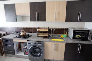 A kitchen with a gas stove, a microwave, a washing machine, and a sink. - Charming Accessible Apartment in Martil, Morocco (Martil)