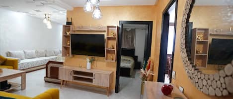 A modern living room with a flat-screen TV, wooden entertainment unit, yellow sofa, and a large mirror.