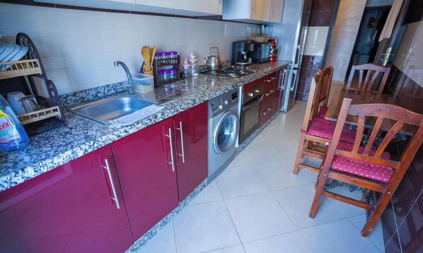 A kitchen with a washing machine, a sink, and a chair. - Charming 2-Bedroom Apartment with Shared Pool in Martil (Martil)