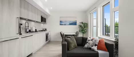 A modern kitchen with integrated appliances, a dining area with a table and chairs, and a living area with a sofa and cushions.
