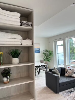A modern living room with a grey sofa, a dining table with chairs, and a large window.