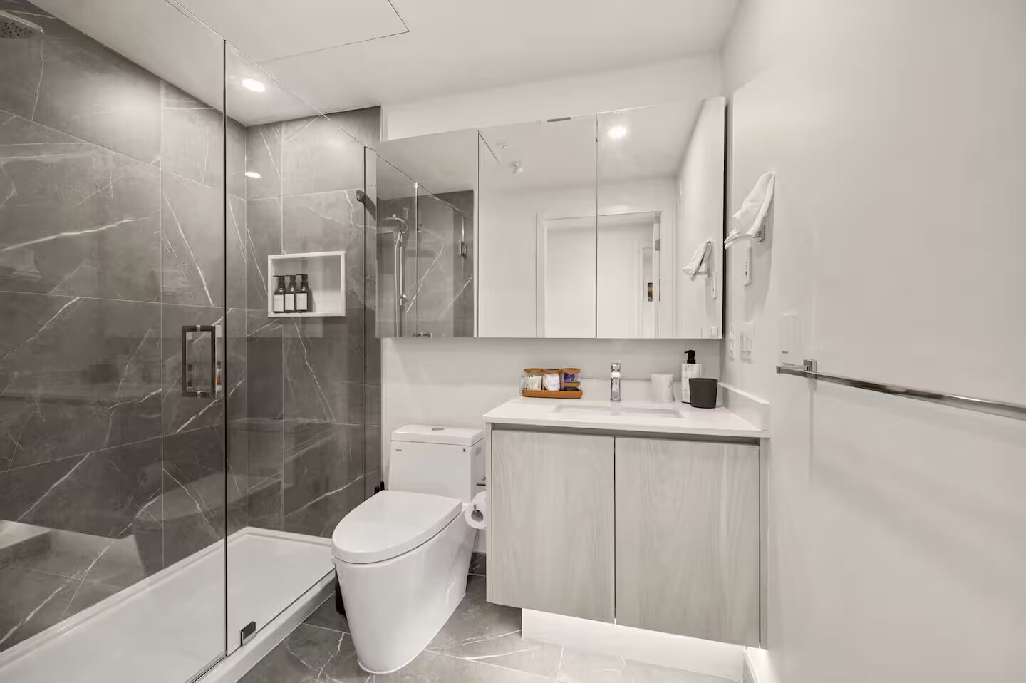 Un baño moderno con cabina de ducha de vidrio, un inodoro y un lavabo con espejo.