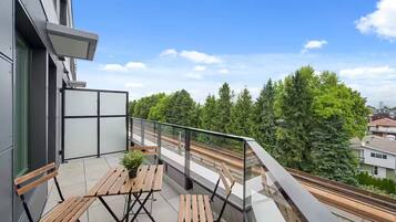 A balcony with a view of a railway track, a bench, and a potted plant.