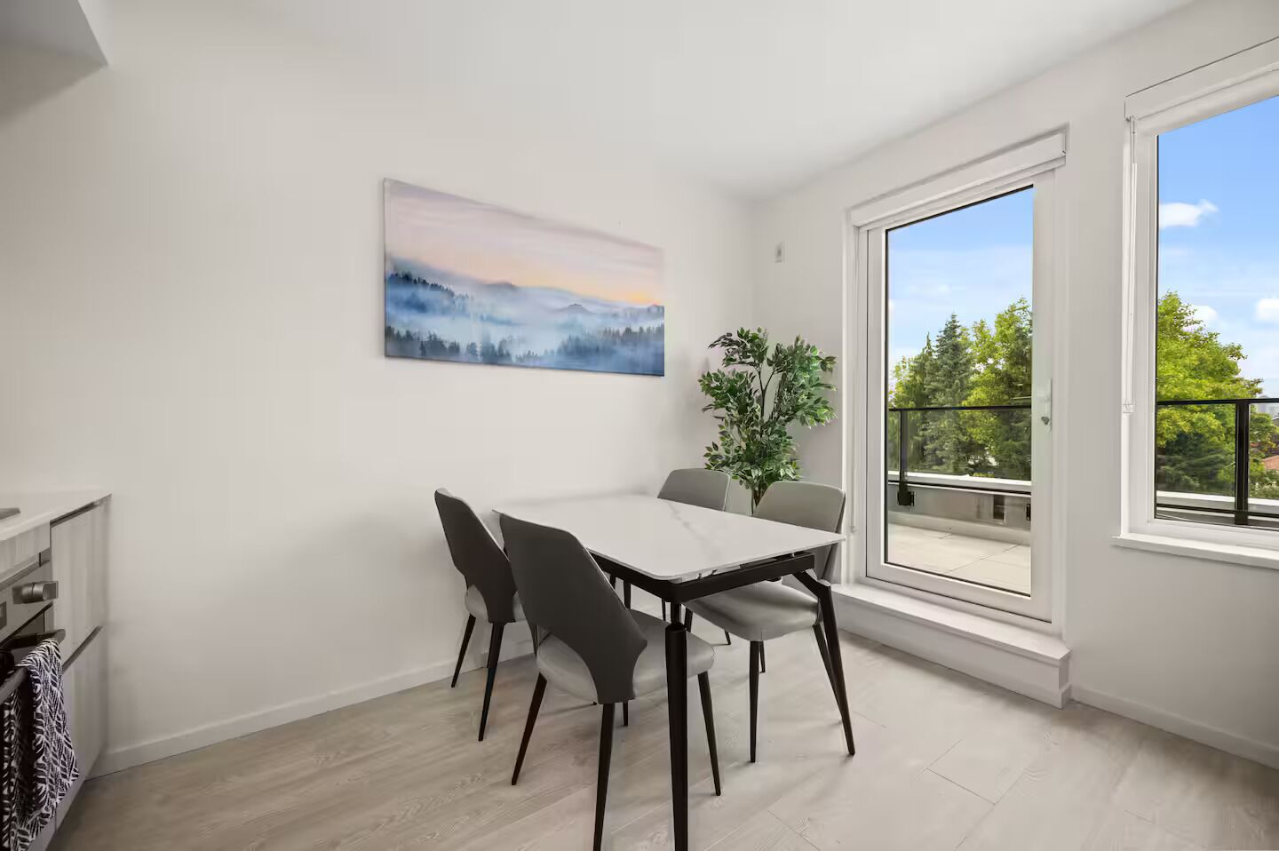 Ein stilvoller Essraum mit einem weißen Tisch, vier Stühlen, einem Gemälde und Blick auf Grün durch ein großes Fenster.