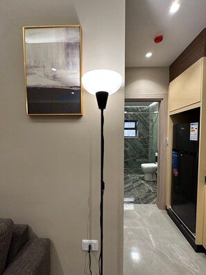 A modern interior with a floor lamp, a framed picture, and a view into a bathroom with a toilet and shower. - 305 AL-NAJEH JRE Apartments For Rent ave (Amman)