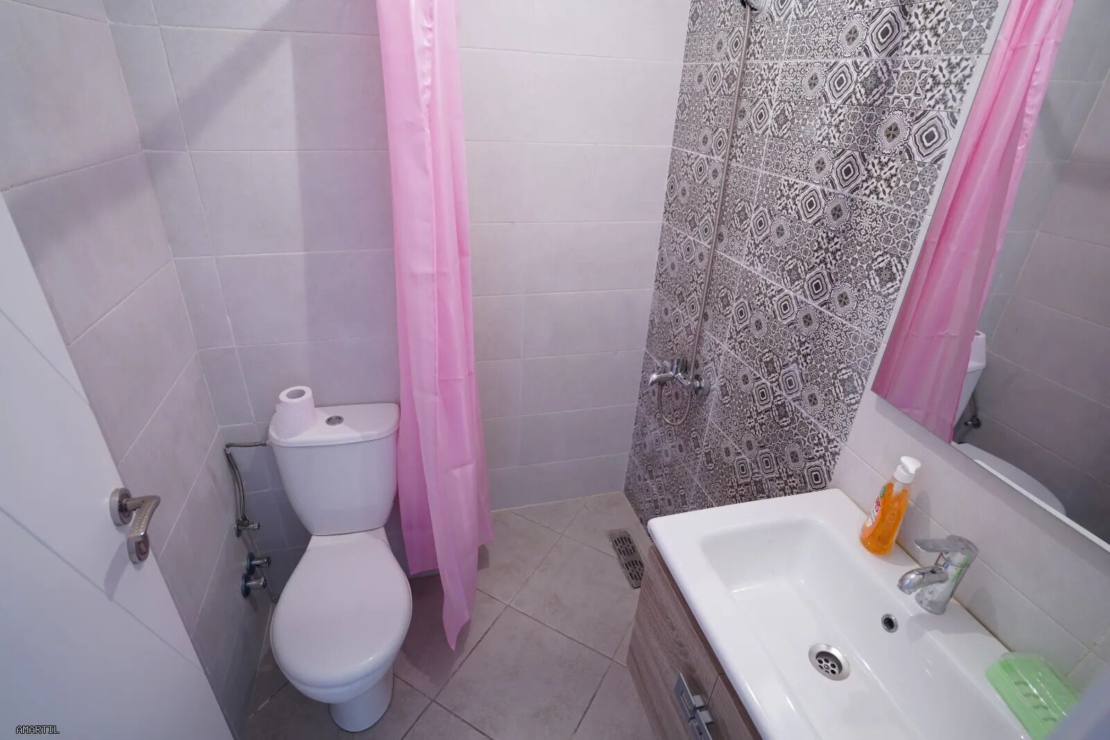 A bathroom with a toilet, a shower with patterned tiles, and a sink with soap.