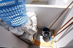 Ein Wäschekorb, ein Mop und ein Eimer in einem schmalen Raum mit weißen Wänden.