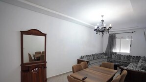 A room with a dining table, chairs, a sofa, a mirror, and a chandelier. - Charming 2-Bedroom Apartment in Martil with City Views (Martil)