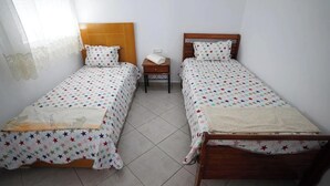 A room with two single beds, each with a star-patterned bedspread and matching pillows. There is a nightstand with a lamp between the beds. - Charming 2-Bedroom Apartment in Martil with City Views (Martil)