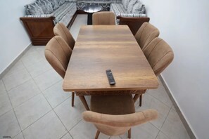Ein Esstisch mit Stühlen, eine Fernbedienung auf dem Tisch und ein gemustertes Teppich im Hintergrund.