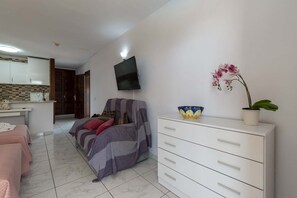 Ein Wohnzimmer mit einer Couch, einem an der Wand montierten Fernseher, einer weißen Kommode und einer Topforchidee.