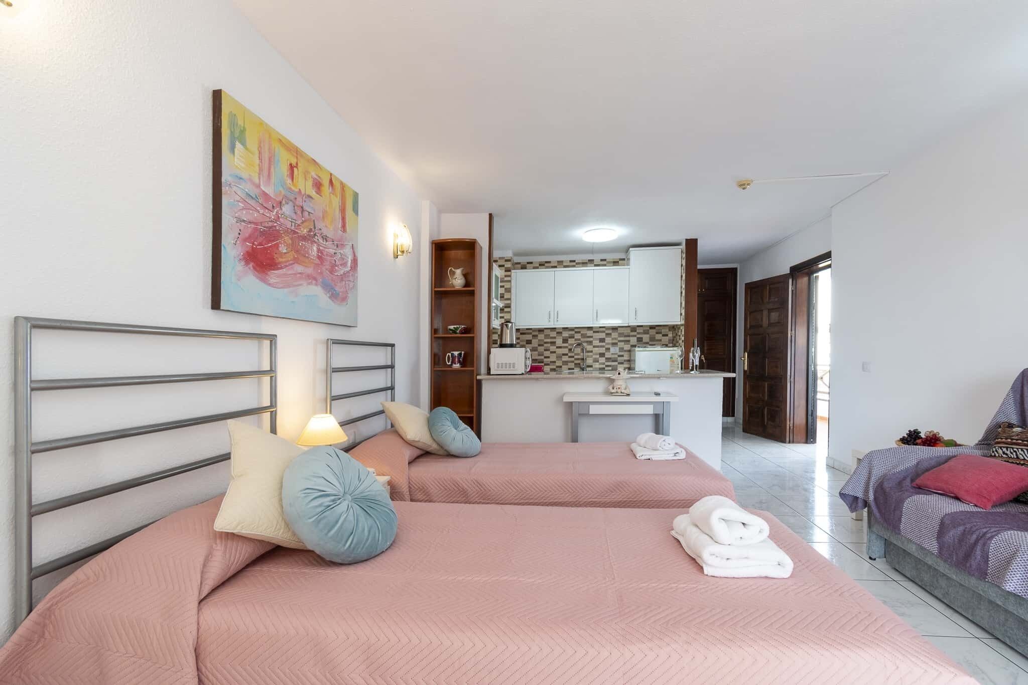 Une chambre d’hôtel avec deux lits, une kitchenette et un tableau au mur.