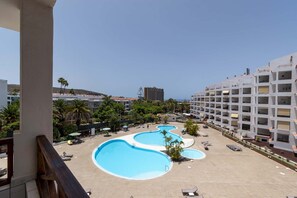 Ein Hotel mit mehreren Schwimmbecken, einer angelegten Grünfläche mit Palmen und Blick auf das Meer.