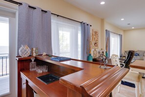 Ein helles Zimmer mit einem Holztisch, einem Sessel, einer Couch und einem Fenster mit Vorhängen.