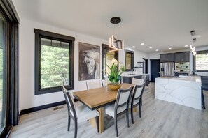 A modern kitchen with a central island, large windows, and a dining area with a wooden table and chairs. - Brand-New Luxury Estate with Expansive Mtn Views! (Donnelly)