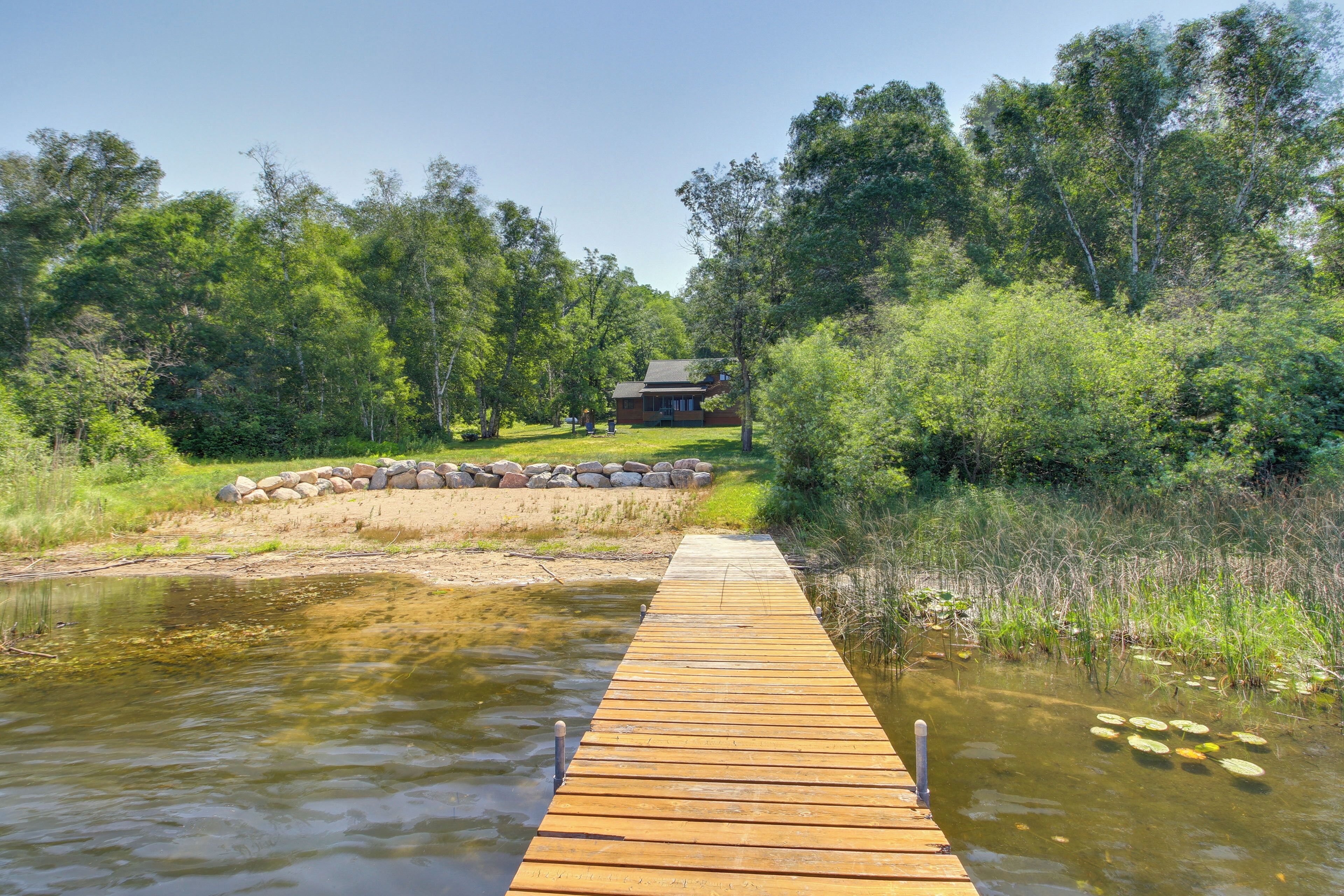 A wooden dock leading to a house surrounded by trees and a body of water.