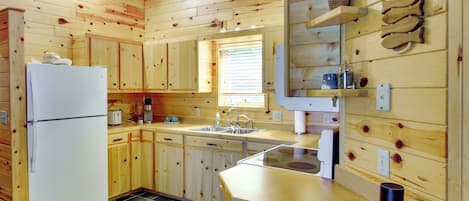 A wooden cabin kitchen with a refrigerator, sink, and wooden cabinets.