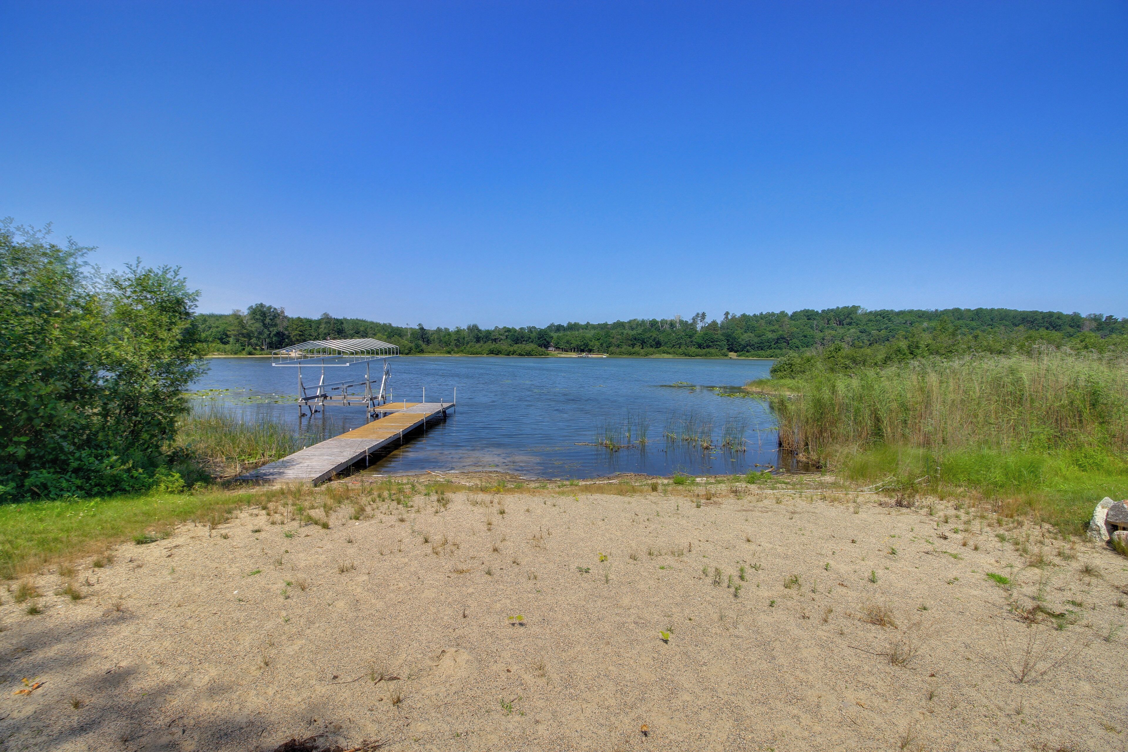 A clear view of a lake with a wooden dock extending into the water, surrounded by grassy areas and dense trees.