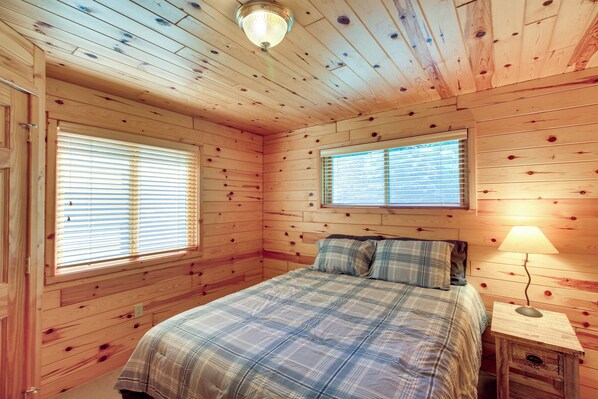 Ein Zimmer aus Holz mit einem Bett, zwei Fenstern und einer Lampe.