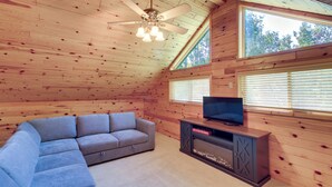 A wooden interior with a sectional sofa, a flat-screen TV on a wooden stand, and a ceiling fan. - Fire Pit & Screened Porch! 3.5-Acre Nevis Retreat (Nevis)