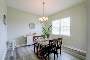 A dining area with a wooden table, chairs, a chandelier, a potted plant, and a window with blinds. - Near Tyndall AFB & the Beach! Panama City Retreat (Panama City)