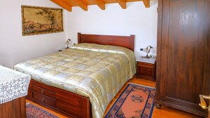 Un dormitorio con cama de madera, mesita de noche, armario, un cuadro en la pared y una alfombra estampada.