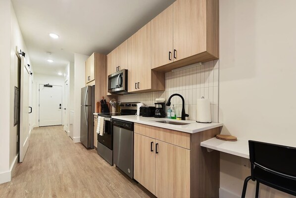 A modern kitchen with wooden cabinets, stainless steel appliances, and a white countertop. - HULU+GYM+PARKING Near Shopping|UPMC|Universities (Pittsburgh)