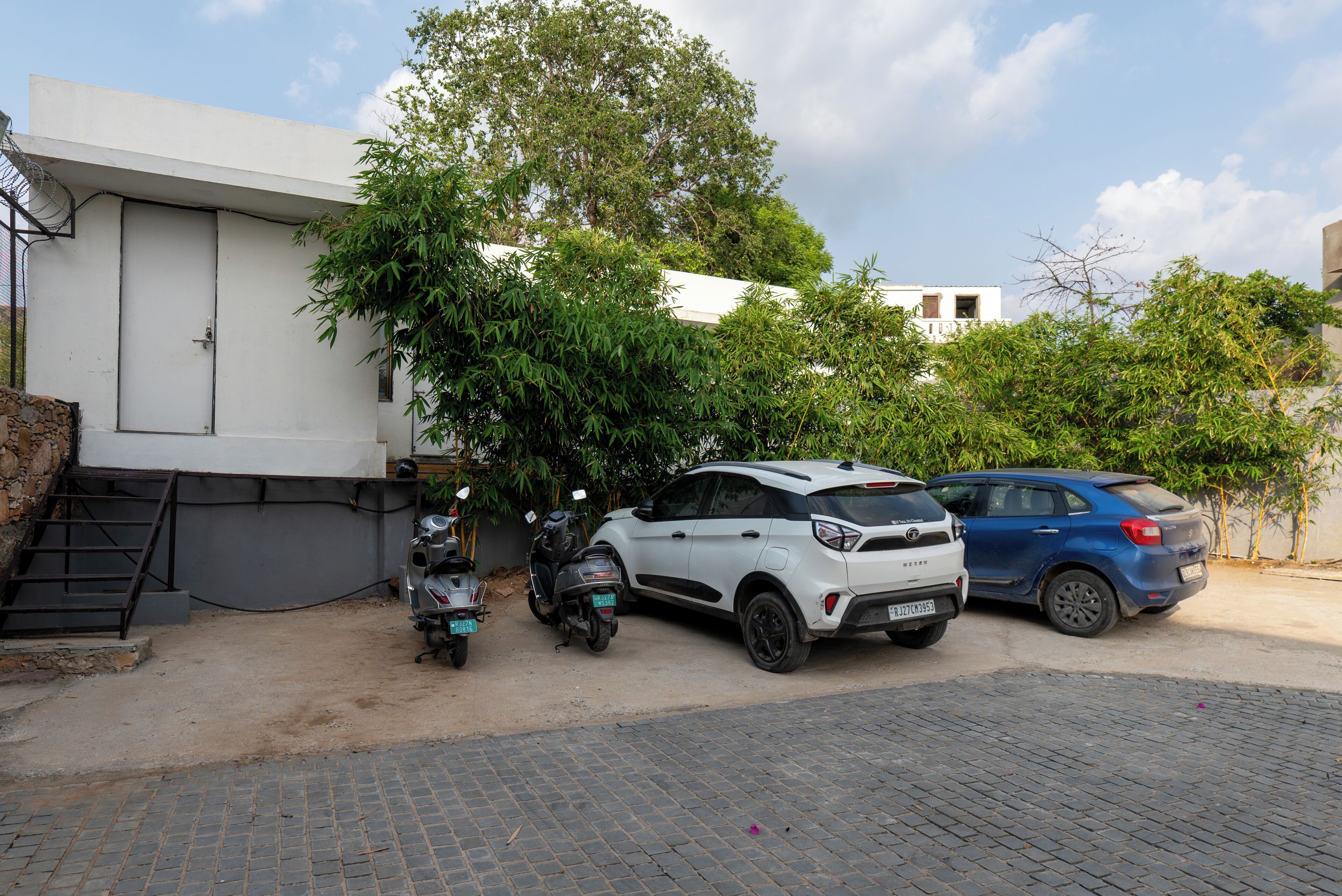 A parking area with two scooters and two cars parked.