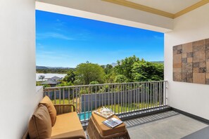 A balcony with a view of a swimming pool, a sofa, and a table with a tray of items. - Miran by the Lake - ELIVAAS Signature (Lakhawali)