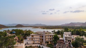 A multi-story building with a flat roof, surrounded by greenery and a river.