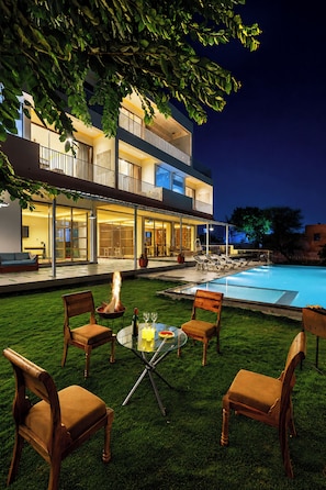 A modern two-story building with a swimming pool, outdoor seating, and a fire pit. - Miran by the Lake - ELIVAAS Signature (Lakhawali)