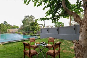Zona de piscina con mesa y sillas, rodeada de vegetación y un muro gris.