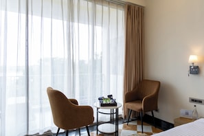 A hotel room with two chairs, a small table, a bed, and a window with curtains.