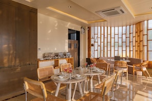 A modern dining area with round tables, wicker chairs, and a buffet station.