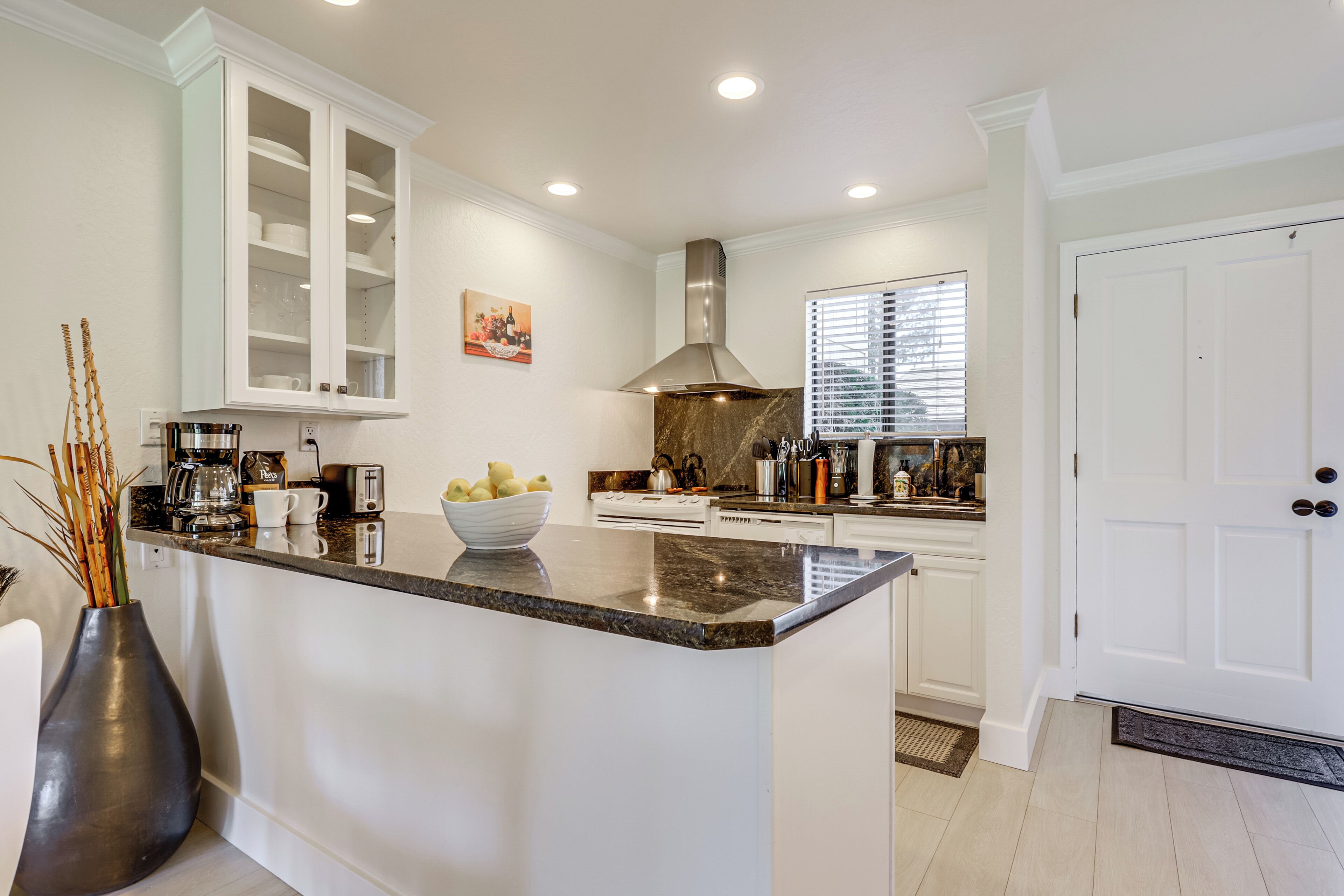 A modern kitchen with white cabinetry, a granite countertop, and a central island with a bowl of lemons.