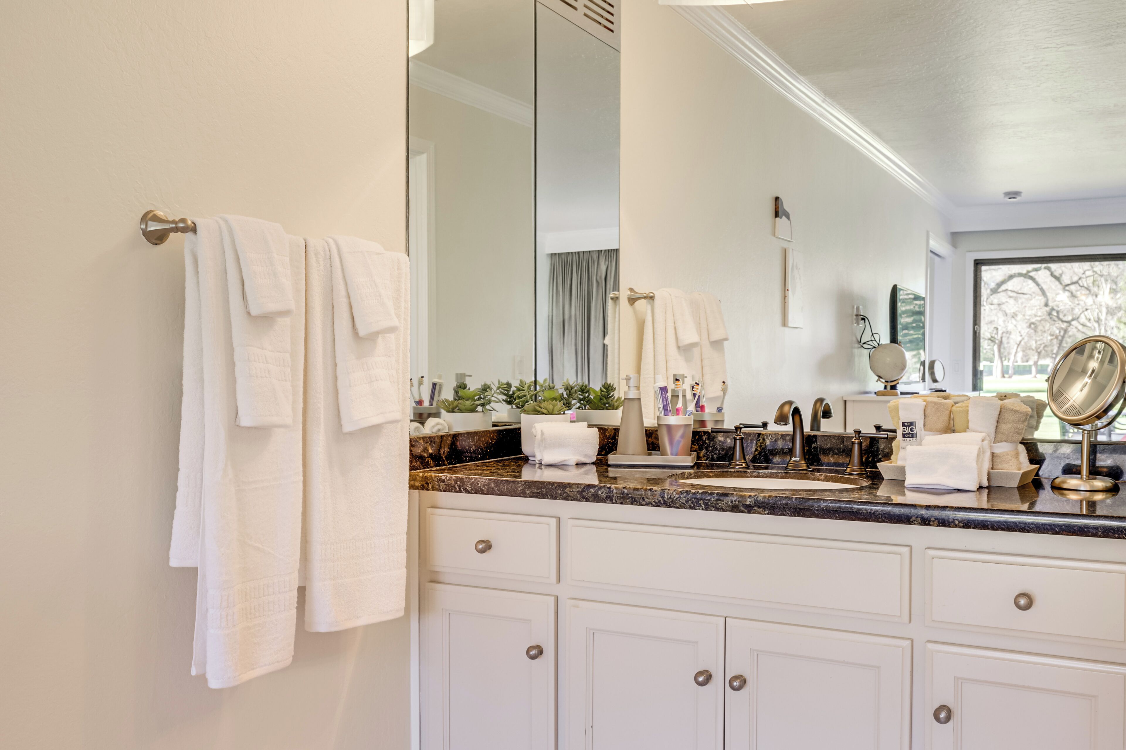 A bathroom with white cabinets, a marble countertop, and a large mirror.